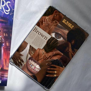 May include: A clear phone case with a collage design. The collage includes the word "Brown" and the text "My Black is Beautiful." It features images of brown skin, gold jewellery, and a close-up of an eye.