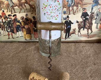 Op de afbeelding: Twee kurken met tekst, een kurkentrekker en een heldere glazen fles met een etiket waarop "Cabernet d'Anjou" staat en dat een bloemenmotief heeft. De fles staat op een bruine jute ondergrond.