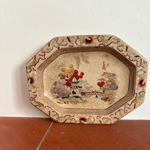 May include: A vintage octagonal ceramic dish with a cream-colored glaze and a hand-painted design of a Chinese garden scene with a bridge, trees, and flowers. The dish has a brown and red border with a geometric pattern.