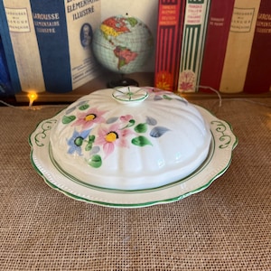 May include: A white ceramic butter dish with a lid. The lid has a floral design with pink, blue, and green flowers. The dish has a green trim.