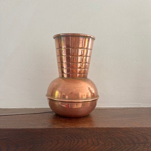 May include: A copper vase with a round base and a flared top. The vase has a hammered texture and a shiny finish.