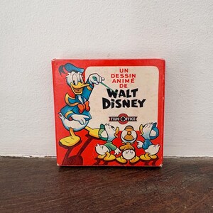 May include: A square red box featuring a graphic of Donald Duck pointing a green stick toward three ducklings. The text reads UN DESSIN ANIMÉ DE WALT DISNEY and FILM-OFFICE. The box has a white central panel and a bright red border with cartoon characters.