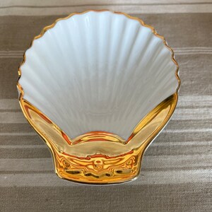 May include: A white porcelain seashell dish with a gold rim and a gold design on the bottom.