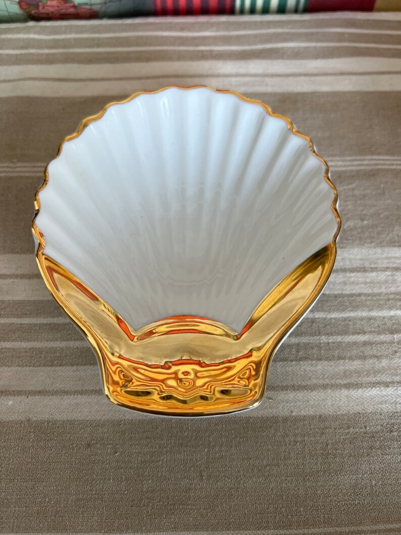 May include: A white porcelain seashell dish with a gold rim and a gold design on the bottom.