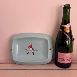 May include: A light blue ceramic ashtray with a walking man graphic and the text "Born 1810 - Still Going Strong". A bottle of Mo&euml;t & Chandon Ros&eacute; Imp&eacute;rial champagne is next to the ashtray.