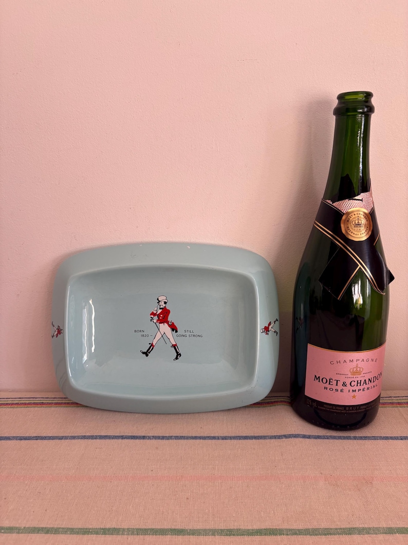 May include: A light blue ceramic ashtray with a walking man graphic and the text "Born 1810 - Still Going Strong". A bottle of Mo&euml;t & Chandon Ros&eacute; Imp&eacute;rial champagne is next to the ashtray.