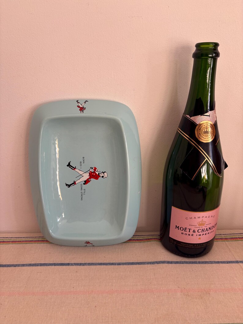 May include: A light blue ceramic ashtray with a red and white illustration of a person riding a horse. The ashtray is next to a bottle of Mo&euml;t & Chandon Ros&eacute; Imp&eacute;rial champagne.