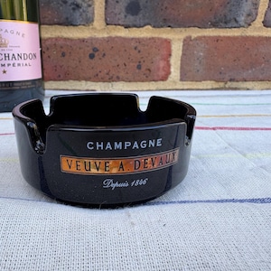 Op de afbeelding: Zwarte asbak van keramiek met gouden opschrift "Champagne Veuve A. Devaux Depuis 1846".
