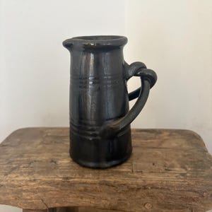 Una brocca vintage in ceramica artistica inglese Dicker Ware con smalto scuro metallico effetto ferro. Manico a doppia corda intrecciata e anelli attorno al corpo.