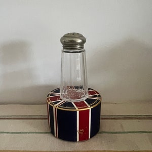 May include: A clear glass salt shaker with a silver top sits on a round, blue, red, and white box with a gold trim. The box has a Union Jack design and the text "CARR'S TABLE WATER CRACKERS" printed on it.