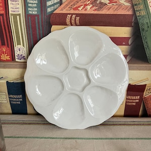 Puede incluir: Un plato de ostras de cerámica blanca con seis hendiduras individuales. El plato está sobre un mantel a rayas.