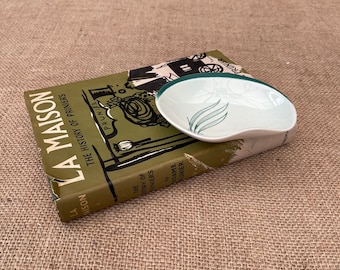Może przedstawiać: Biała ceramiczna miseczka z zielonym rantem i zielonym wzorem liści. Miseczka leży na zielonej książce z tytułem "La Maison" i tekstem "The History of Prunier's".