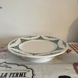 Könnte beinhalten: Ein weißer Kuchenständer aus Keramik mit einem grünen floralen Design am Rand. Der Ständer hat eine erhöhte Basis.