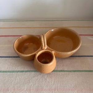 May include: A brown ceramic serving dish with three sections. The dish has a handle and is ideal for serving dips, snacks, or appetisers.