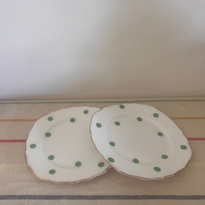 Puede incluir: Dos platos de cerámica blanca con borde festoneado y ribete dorado. Los platos están decorados con lunares verdes.