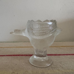 May include: A clear glass egg cup shaped like a bird with a textured surface.