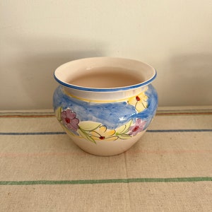May include: A white ceramic planter with a blue background and a floral design in shades of yellow, pink, and purple.
