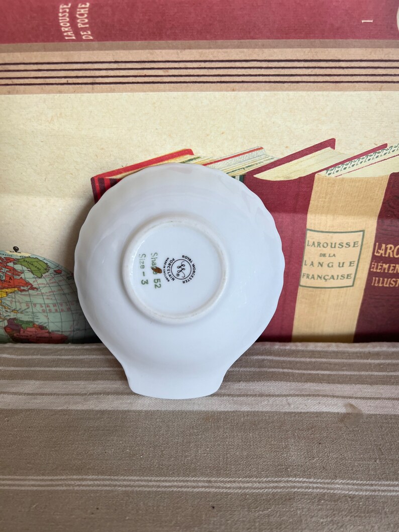 May include: White porcelain dish with a scalloped edge. The bottom of the dish has a gold and green logo that reads "Worcester Royal Porcelain" and "Size 3 Shape 52".