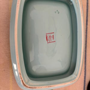 May include: The inside of a light blue ceramic dish with a white rim. The dish has a red and white label that reads "Waite & Son, London, England".