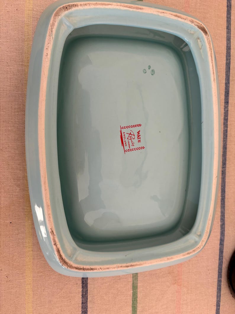 May include: The inside of a light blue ceramic dish with a white rim. The dish has a red and white label that reads "Waite & Son, London, England".