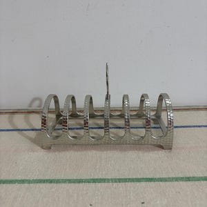 May include: Silver-toned metal bread rack with a hammered finish and five slots. The rack has a handle on the top.