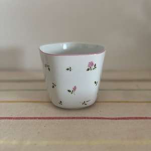 May include: A white ceramic mug with a pink rim and a floral pattern of small pink roses and green leaves.