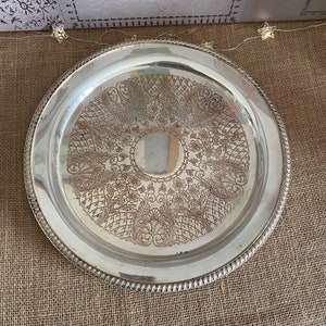 May include: A silver serving tray with a decorative embossed design of flowers and leaves. The tray has a raised rim and a smooth, polished surface.
