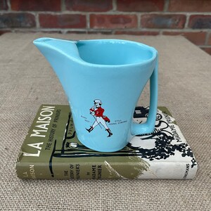 May include: A light blue ceramic jug with a handle. The jug features a Johnnie Walker logo with the text "Born 1820" and "Still Going Strong".