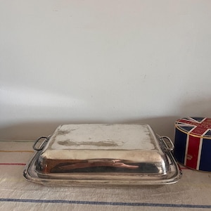 May include: A silver serving dish with two handles. The dish is rectangular and has a shiny, reflective surface.