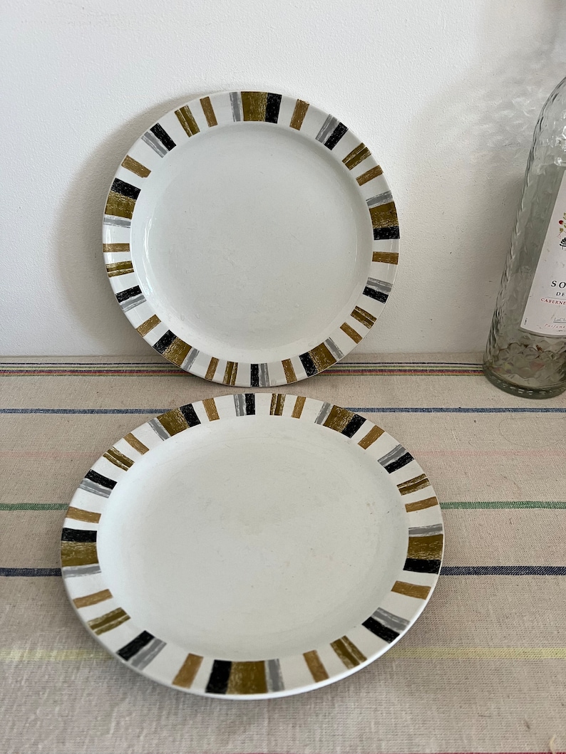Peut inclure: Deux assiettes en c&eacute;ramique blanche avec un motif ray&eacute; noir, or et argent autour du bord.