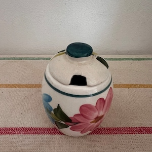 May include: A white ceramic sugar bowl with a floral design. The bowl has a lid with a small hole in the top. The flowers are pink, blue, and green.