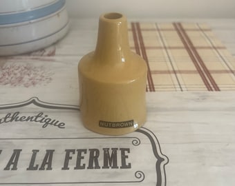 May include: A small, yellow ceramic funnel with the word "NUTBROWN" printed on the bottom. The funnel is sitting on a table with a checkered pattern.