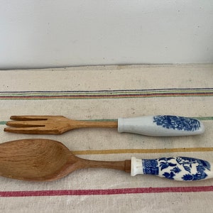 May include: A wooden salad serving set with a blue and white porcelain handle on each piece. The fork and spoon have a natural wood finish.