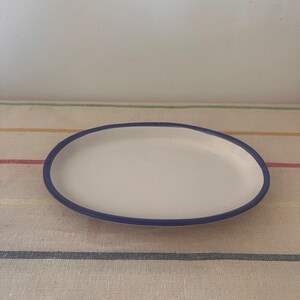 May include: A white oval ceramic serving dish with a dark blue rim.