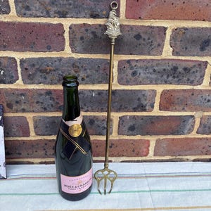 Könnte beinhalten: Ein goldfarbener Flaschenöffner aus Metall mit einem Schiffsdesign auf der Oberseite. Der Flaschenöffner befindet sich neben einer Flasche Moët & Chandon Rosé Impérial Champagner.