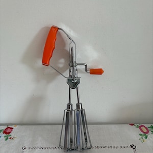 An original vintage retro  stainless steel egg beater hand whisk with and orange plastic handle