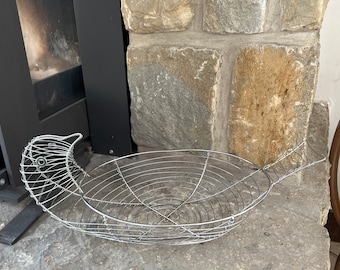 May include: A silver wire basket shaped like a bird with a round base and a handle. The basket is sitting on a stone surface.