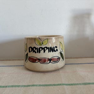 以下が含まれることがあります： 茶色、緑、黄色の花柄が描かれた白い陶器の壺。壺には黒い文字で「DRIPPING」と書かれている。