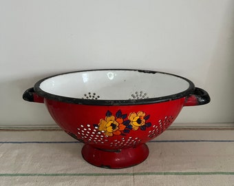 A solid yet well used  red and white vintage enamel colander with a floral design