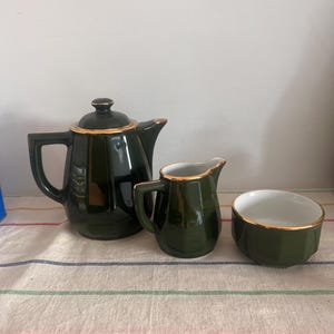 May include: A green tea set with gold trim. The set includes a teapot, creamer, and sugar bowl.