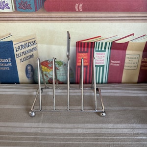 Un elegante soporte para tostadas o cartas de cuatro rebanadas gruesas, triangular y plateado, de estilo victoriano, perfecto para alegrar su mesa de desayuno.