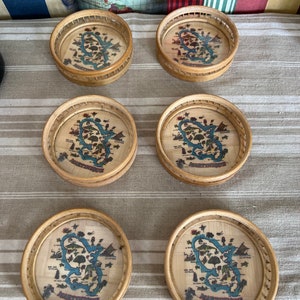 May include: Six round woven bamboo coasters with a map of Martinique printed on the top. The coasters are brown and have a natural woven texture.