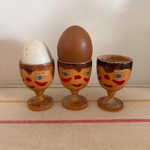 A collectible  set of three early 20th century retro Norwegian Drammen varnished  wooden painted egg cups with a face design