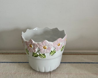 May include: White ceramic planter with a scalloped rim and pink and green floral design.