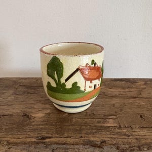 Puede incluir: Una taza de cerámica blanca con un asa negra y el texto "But First, Coffee" en negro y negrita. La taza está sobre una superficie de madera. La taza mide aproximadamente 10 cm de alto.