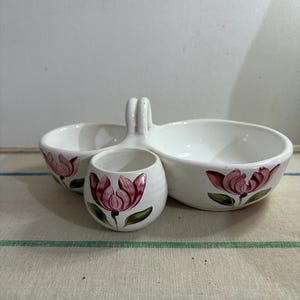 May include: White ceramic serving dish with two bowls and a small cup. The dish has a handle and is decorated with pink flowers.