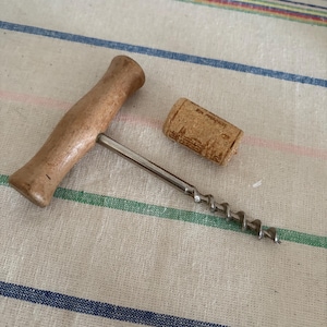May include: A corkscrew with a wooden handle, a metal spiral and a cork on a striped fabric background.