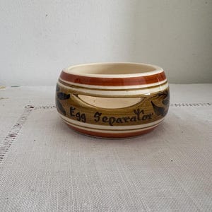 Puede incluir: Un separador de huevos de cerámica marrón y blanco con las palabras "Egg Separator" escritas en el lateral.