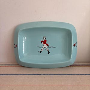 May include: A light blue ceramic ashtray featuring a walking man graphic and the text "Born 1820 - Still Going Strong".
