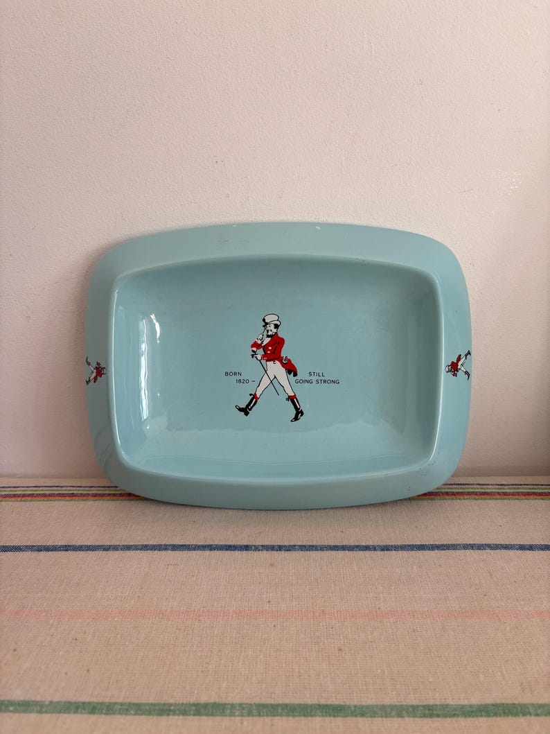 May include: A light blue ceramic ashtray featuring a walking man graphic and the text "Born 1820 - Still Going Strong".
